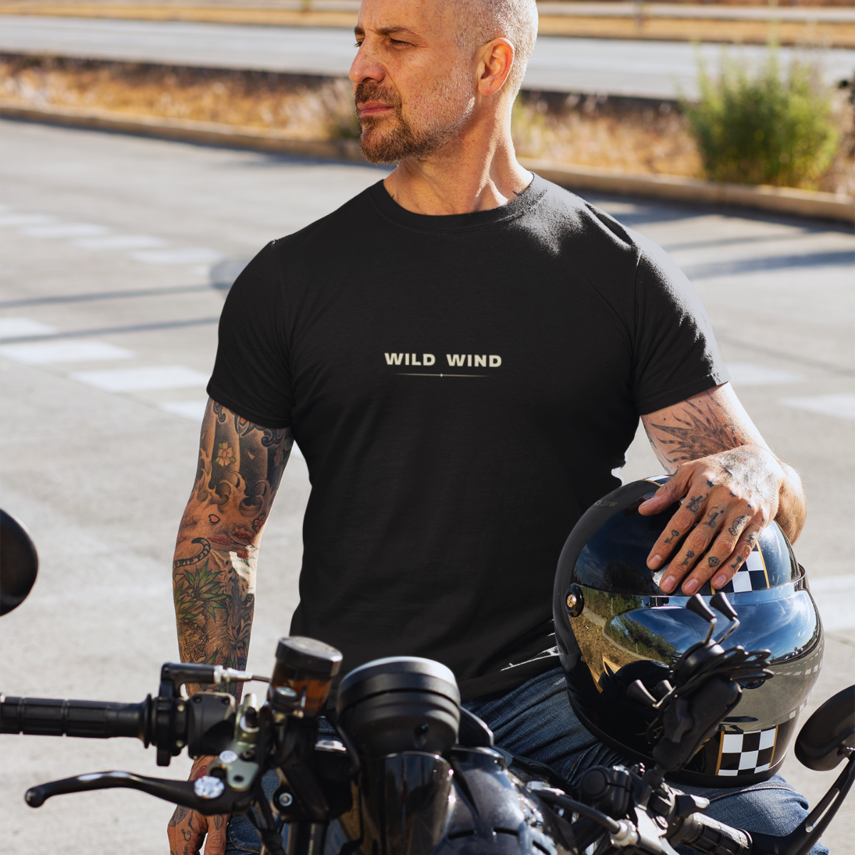 Man wearing a black t-shirt with 'WILD WIND' text, sitting on a motorcycle.