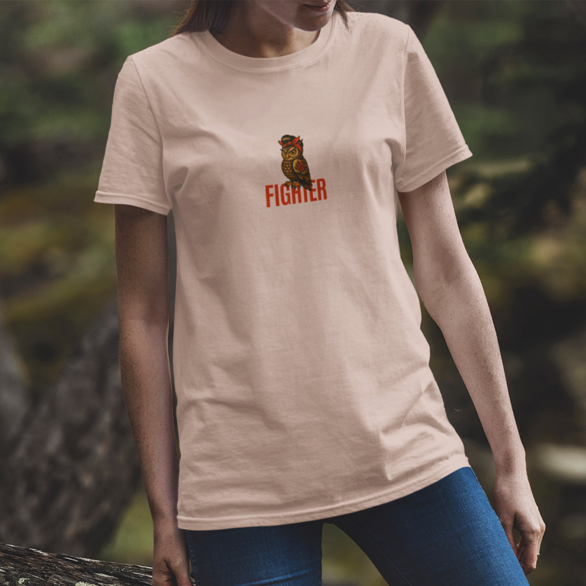 woman  wearing a beige t-shirt with a graphic and the word 'FIGHTER' on it, standing outdoors.