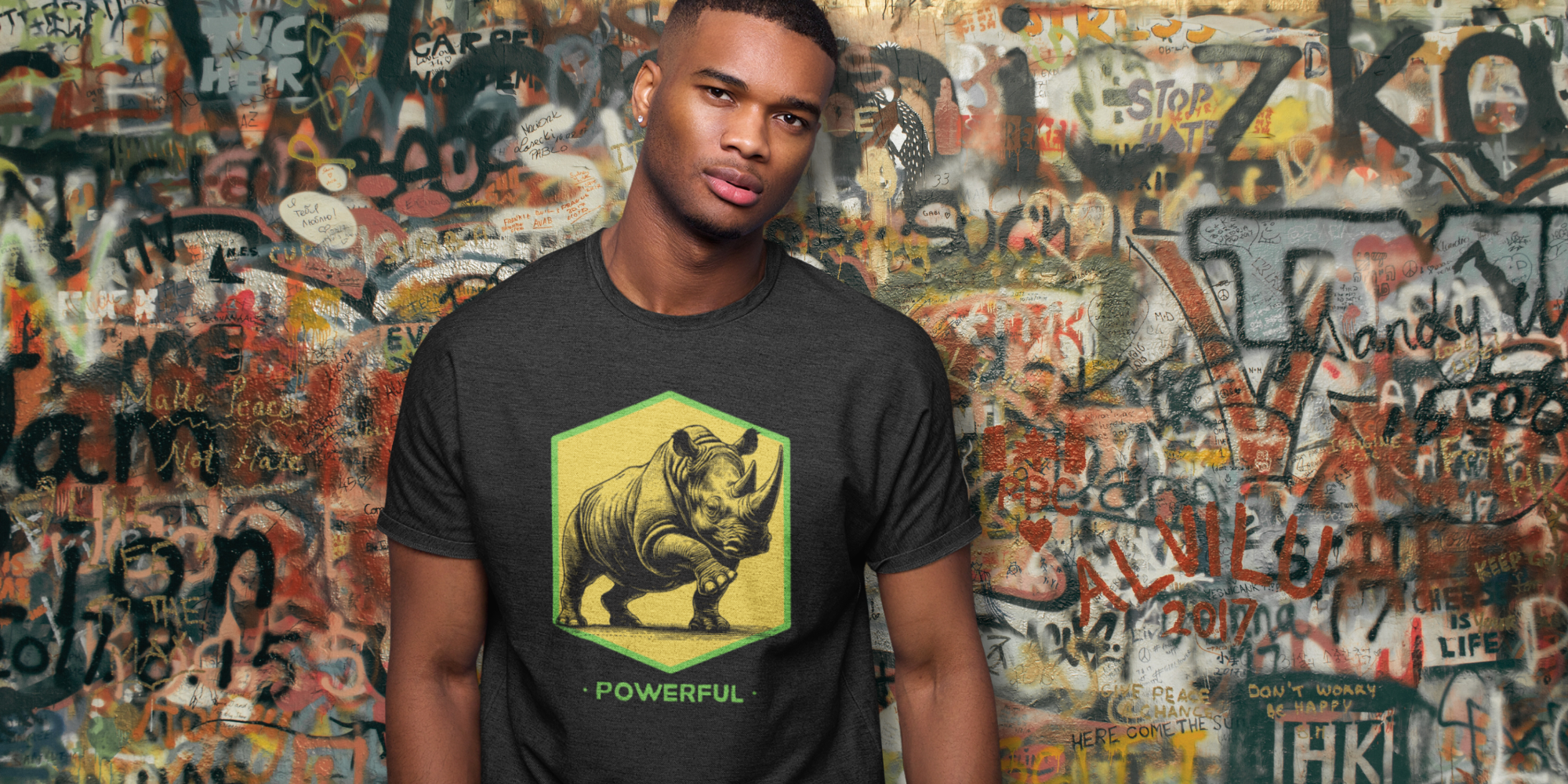 Man wearing a black t-shirt with a rhino graphic and 'Powerful' text, standing in front of a graffiti-covered wall.